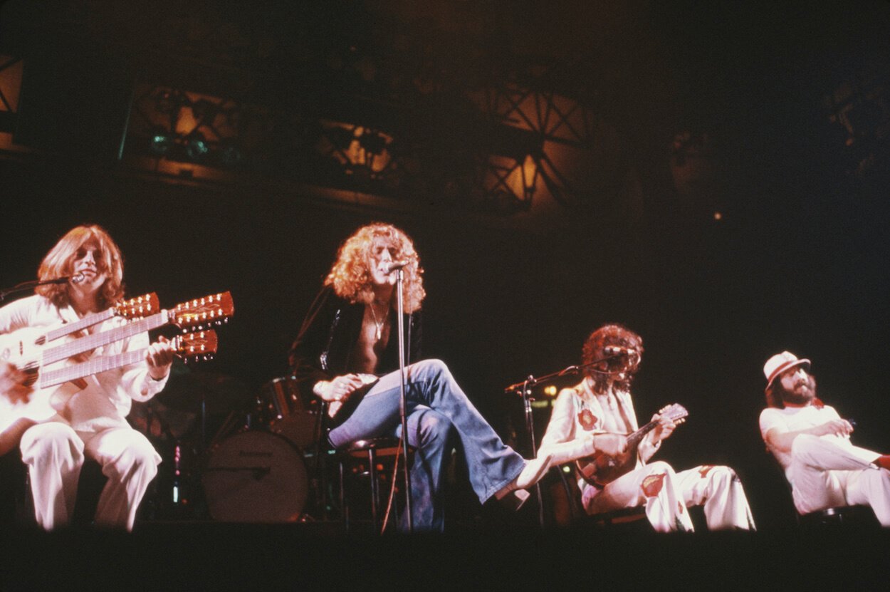 Led Zeppelin members (from left) John Paul Jones, Robert Plant, Jimmy Page, and John Bonham sit in chairs at the front of the stage during a 1977 concert.