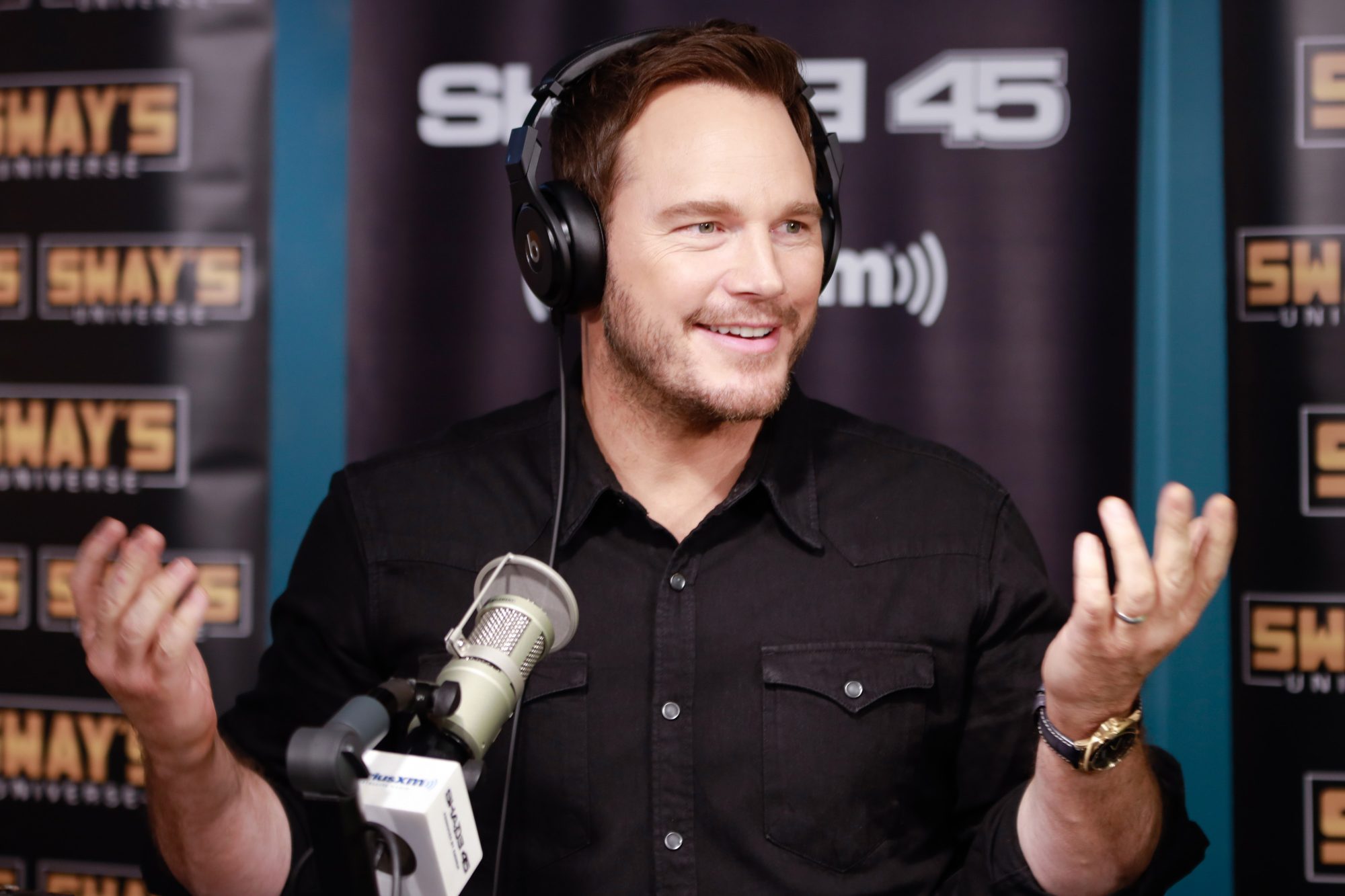 'Live with Kelly' Chris Pratt holding his hands up, wearing headphones, in front of a microphone.