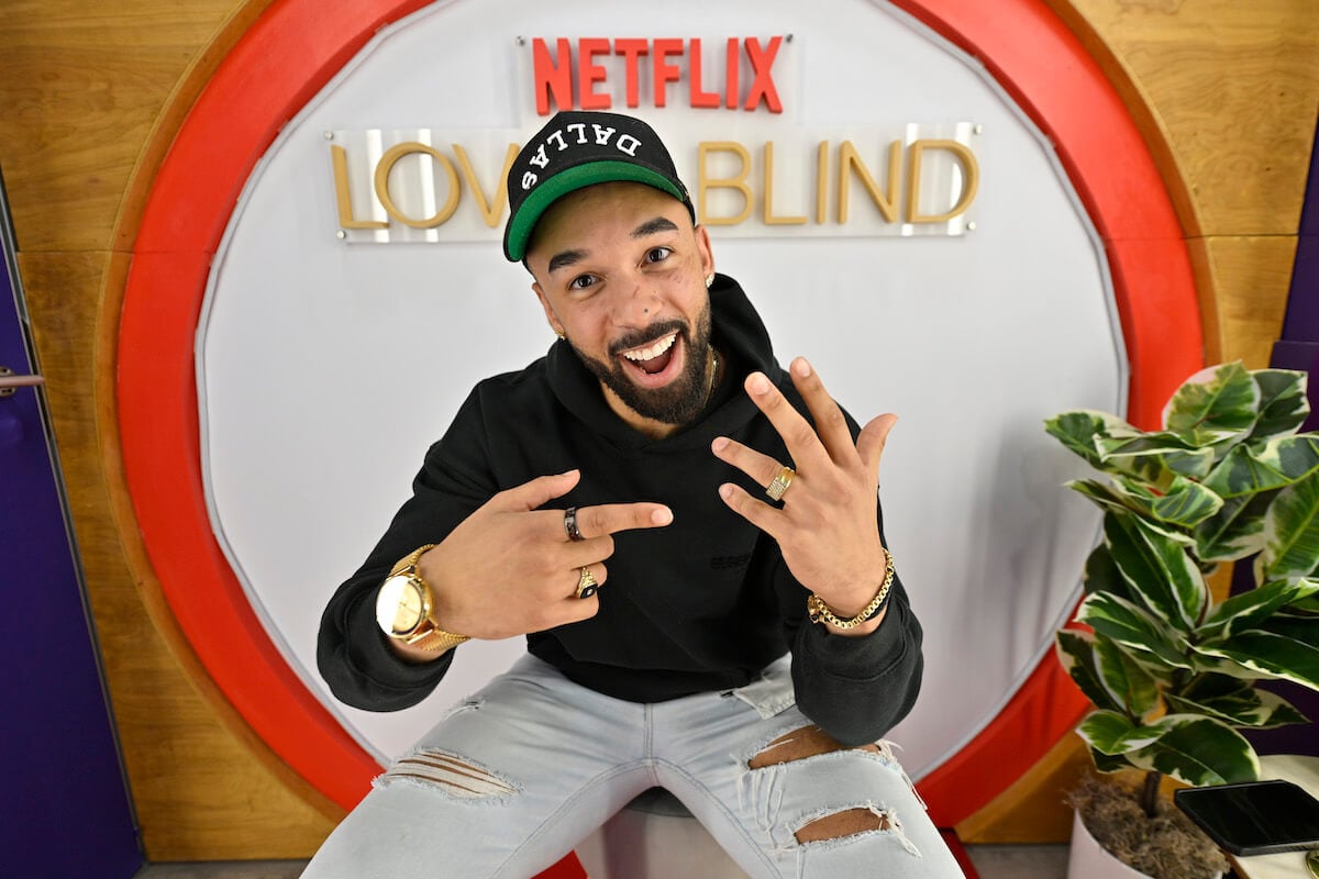 "Love Is Blind" star Bartise Bowden poses on set by smiling and pointing to an engagement ring on his left hand.