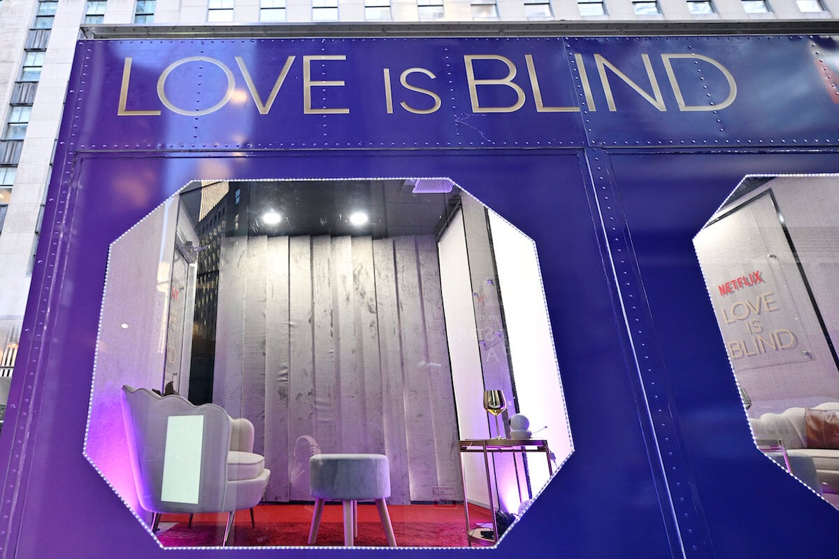 An outside view of a purple 'Love is Blind' pod with a large window, and small table and chairs inside