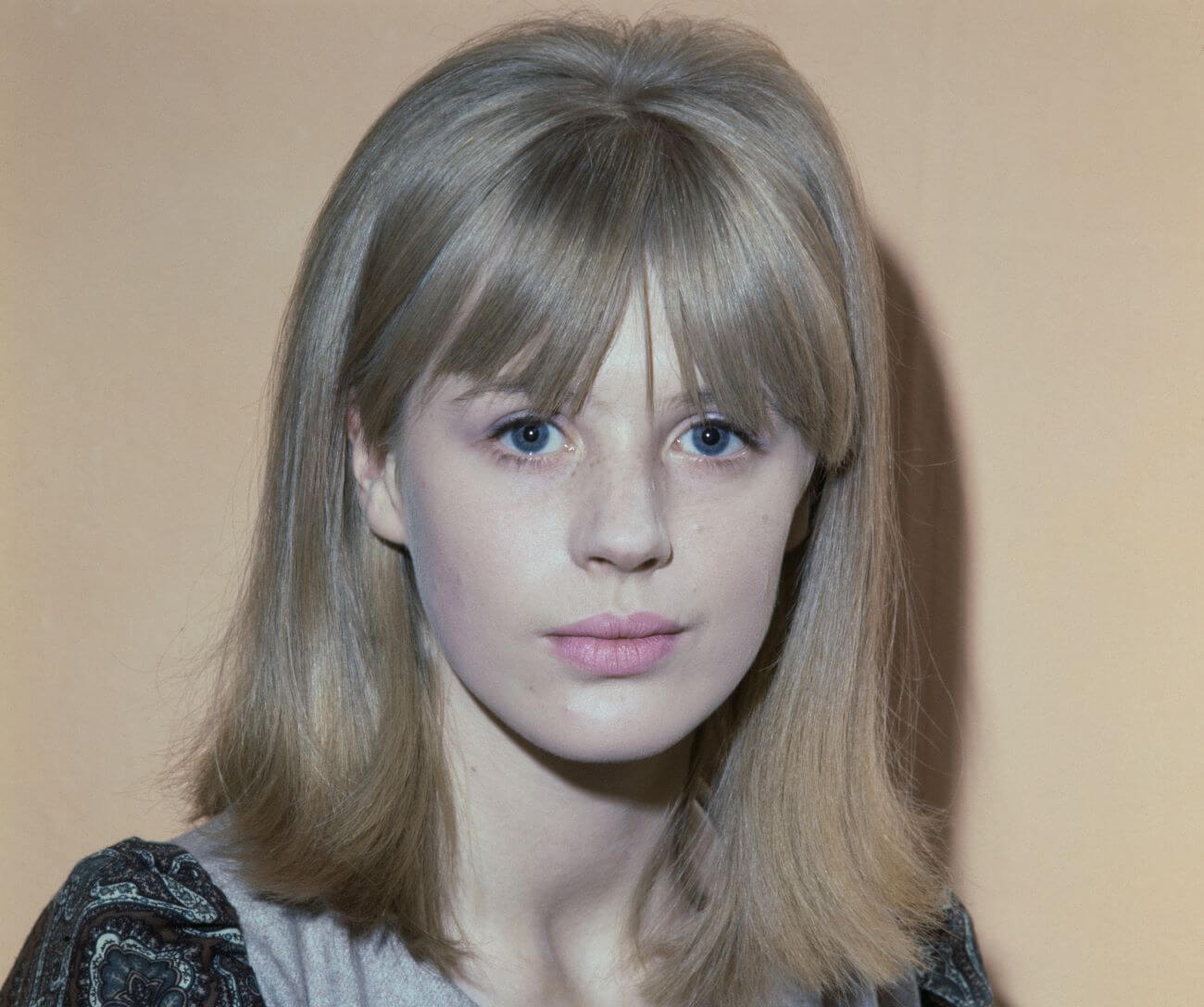 Marianne Faithfull poses in front of a tan wall.