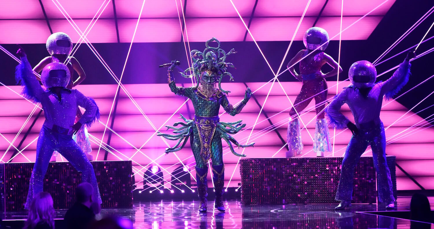 Medusa singing in the center of a stage against a purple background 'The Masked Singer' Season 9.