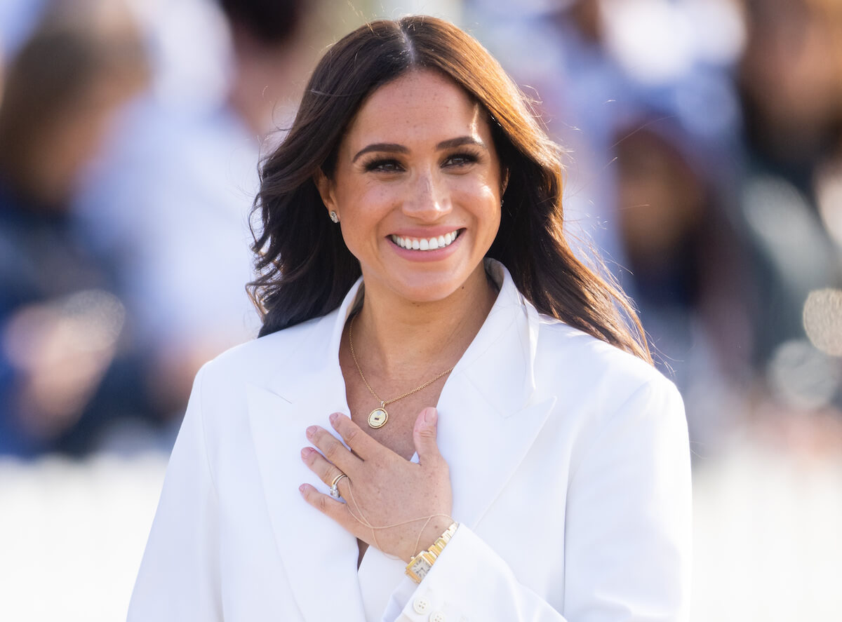 Meghan Markle smiling, holding her hand to her chest