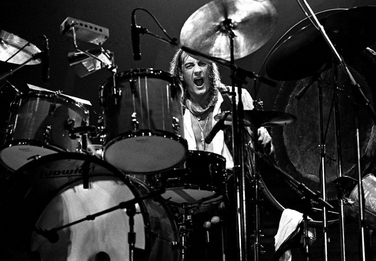 A black and white picture of Mick Fleetwood playing the drums.