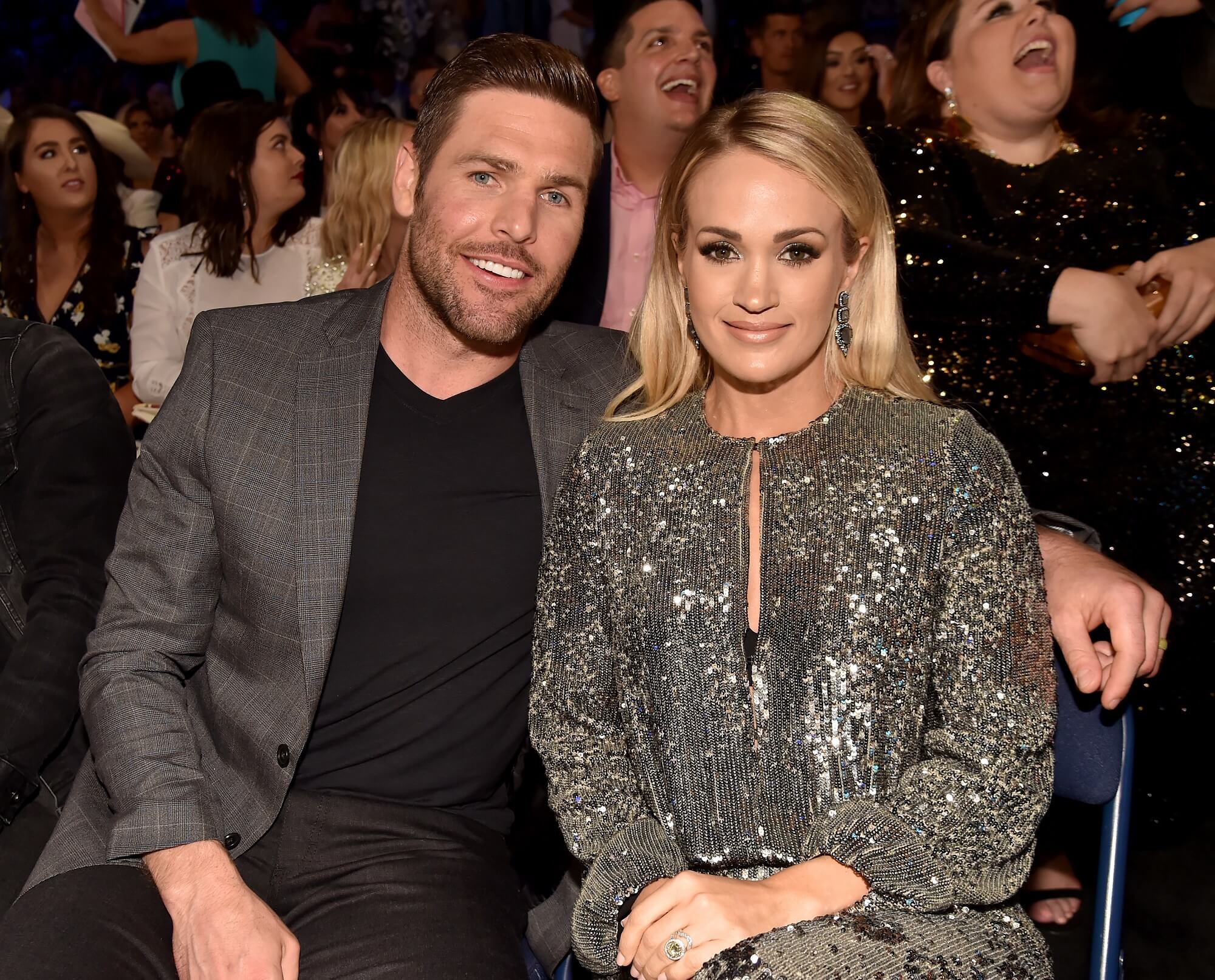 Mike Fisher and Carrie Underwood sit beside each other and look at the camera