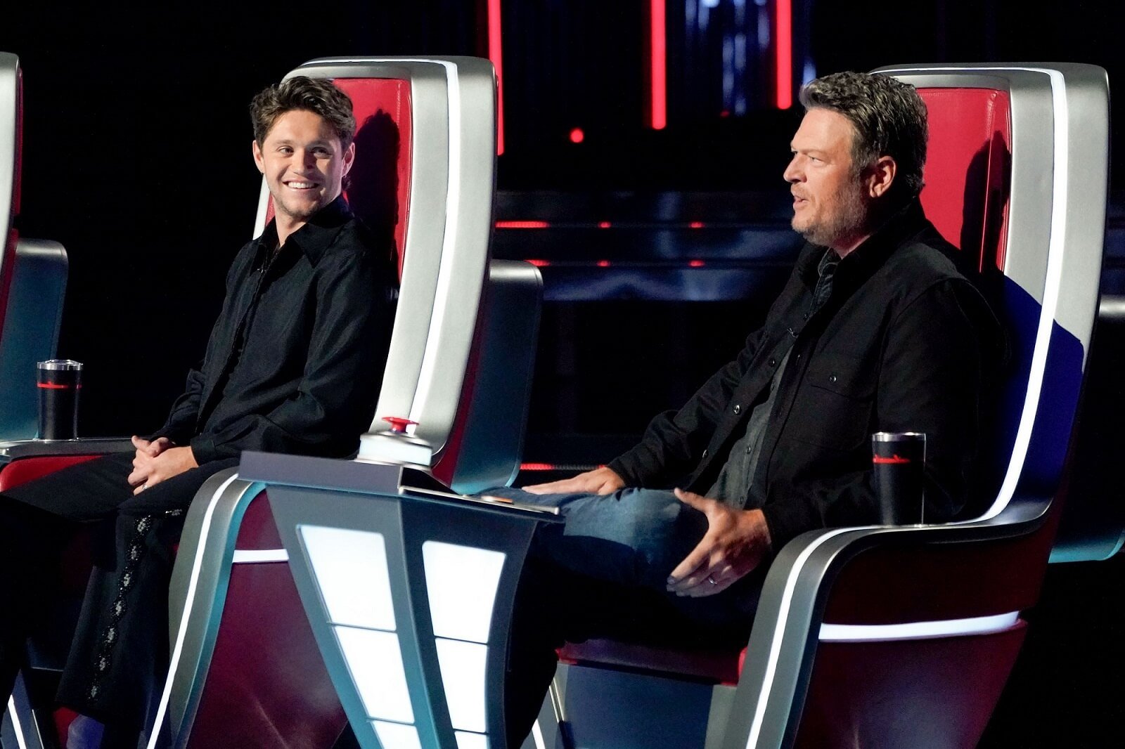 Niall Horan smiles at Blake Shelton while they sit beside each other on 'The Voice'