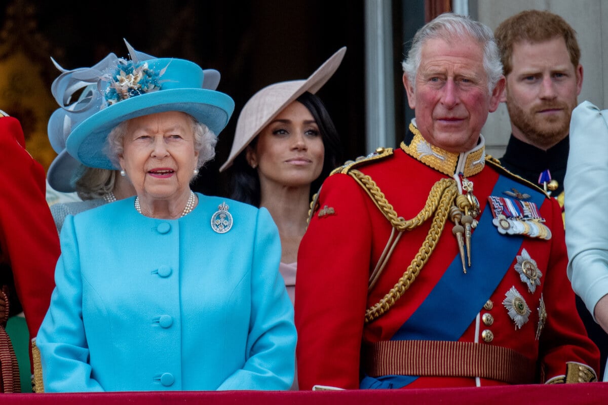 Prince Harry and Meghan Markle, whom a commentator says may have already RSVPd to the coronation, stand behind Queen Elizabeth II and King Charles III