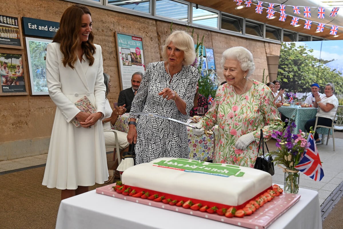 Queen Elizabeth cuts a cake standing next to Kate Middleton and Camilla Parker Bowles