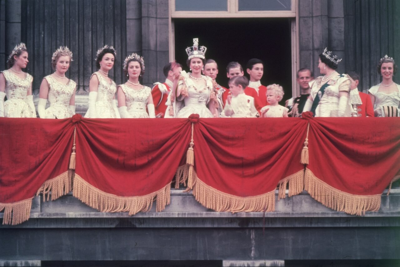Queen Elizabeth II waves to the crowd from the balcony at Buckingham Palace after her coronation in 1953. Her children Prince Charles and Princess Anne stand with her.