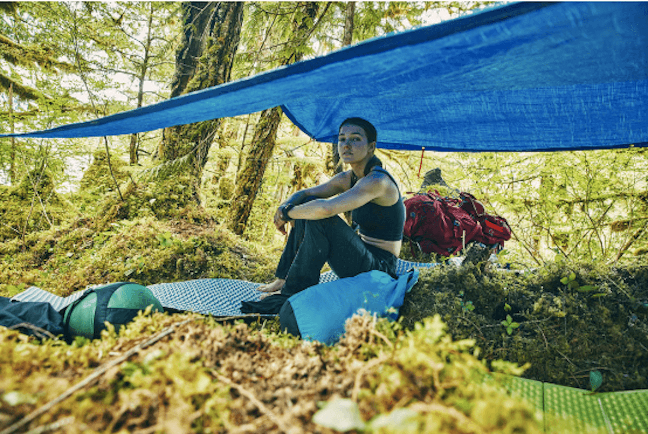 Bella Crane sits in the woods under a blue tarp on 'Race to Survive Alaska'.