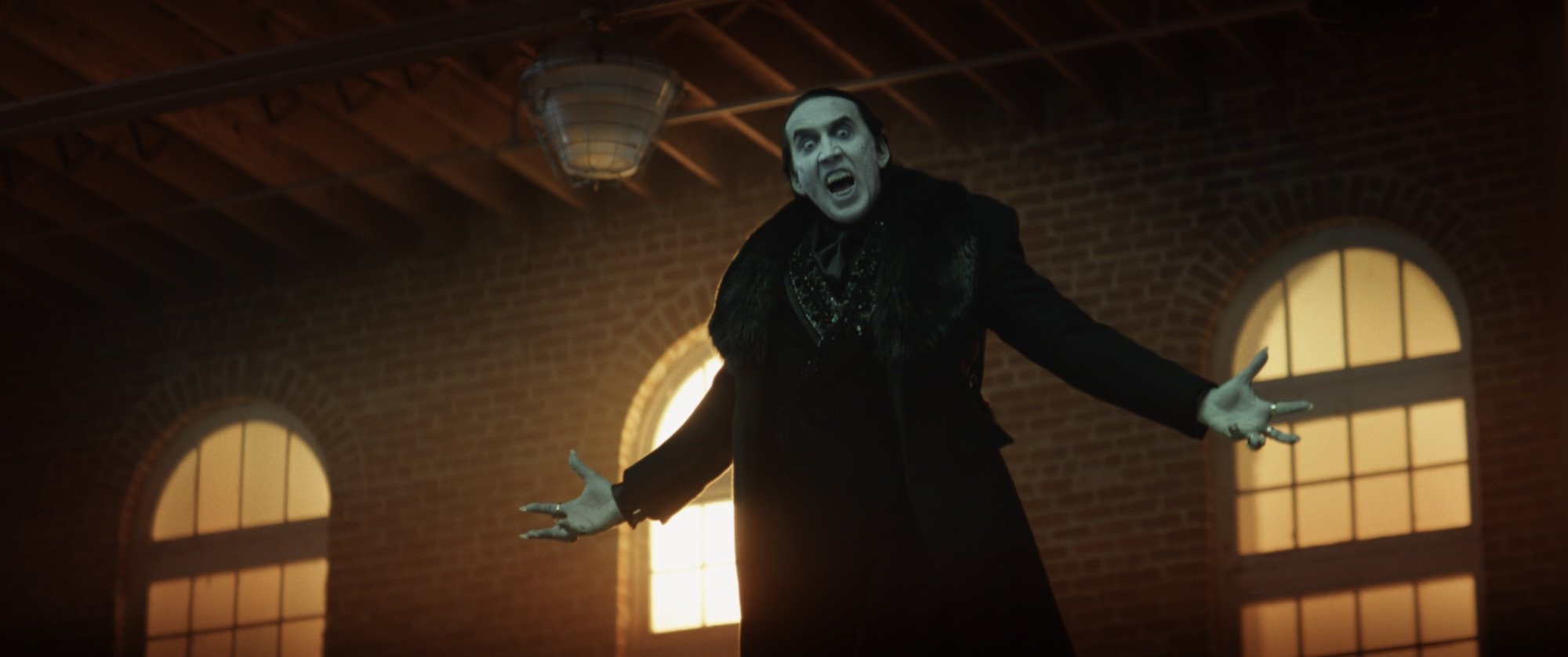 'Renfield' Nicolas Cage as Dracula levitating in the air, with his arms outreached. He's showing his vampire teeth.