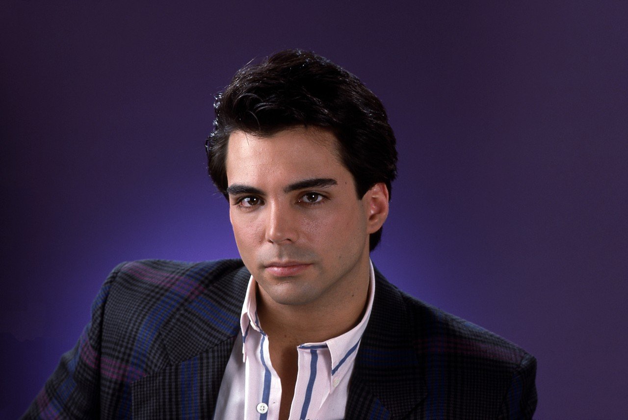 Richard Grieco poses in a blazer and shirt against a purple background. 