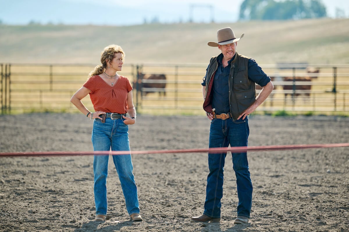 Nancy Travis, in a red shirt, standing next to man in a cowboy hat in the Hallmark series Ride
