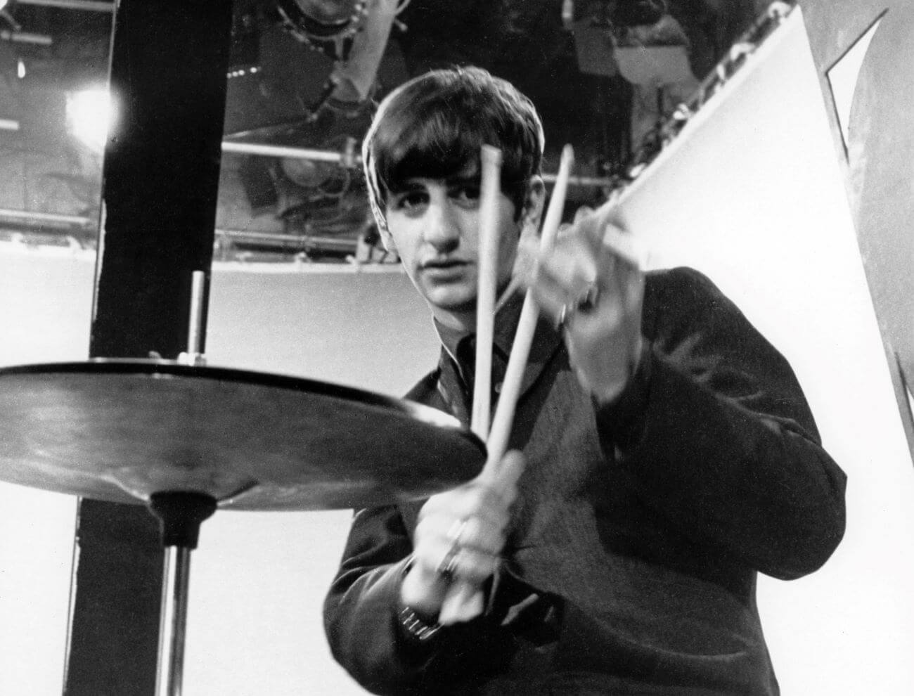 A black and white picture of Ringo Starr sitting at his drum set and holding drum sticks.