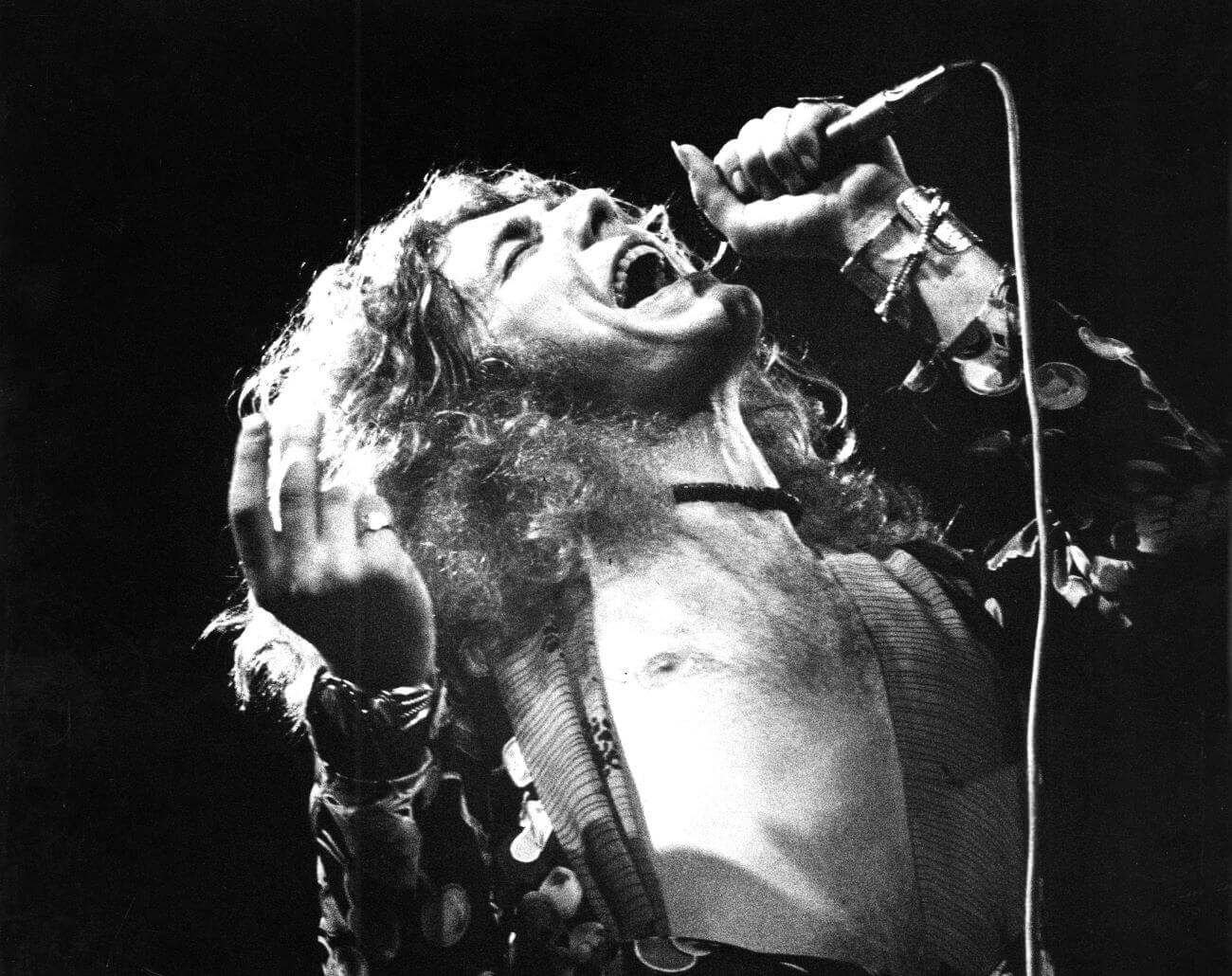 A black and white picture of Robert Plant leaning backward and singing into a microphone.