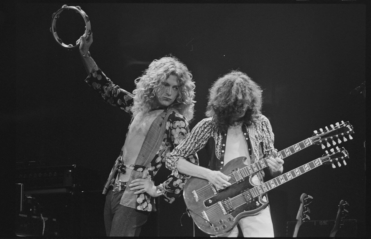 A black and white picture of Robert Plant holding a tambourine and Jimmy Page playing a double neck guitar.