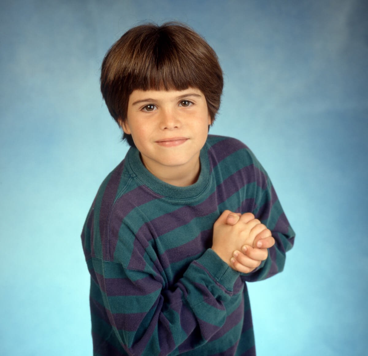 Ross Malinger as a child standing with his hands clasped together