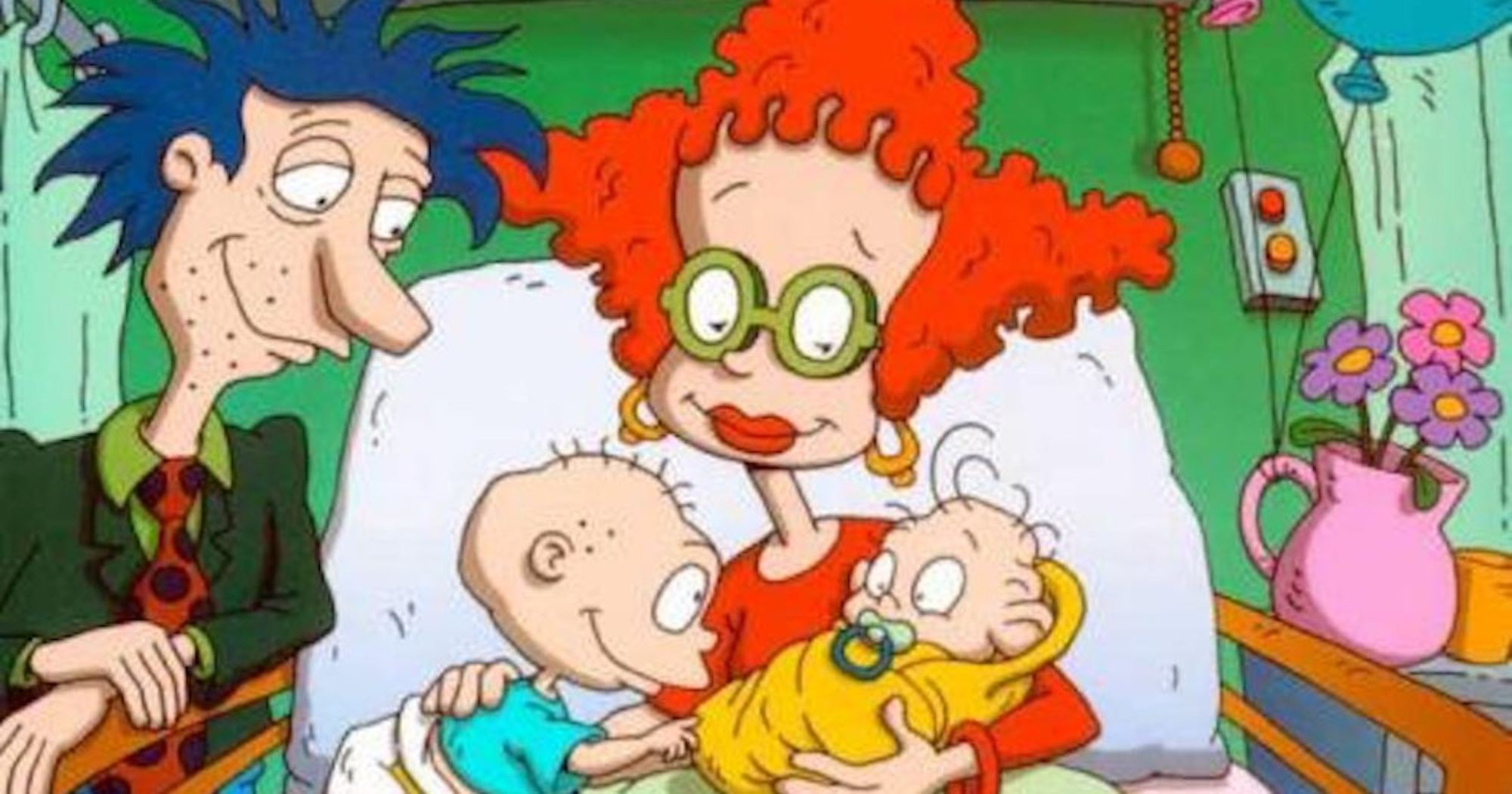 'Rugrats' parents Stu and Didi with Tommy and Dil Pickles. Didi is laying down in a hospital bed, holding the babies, while Stu is standing next to the bed, smiling.