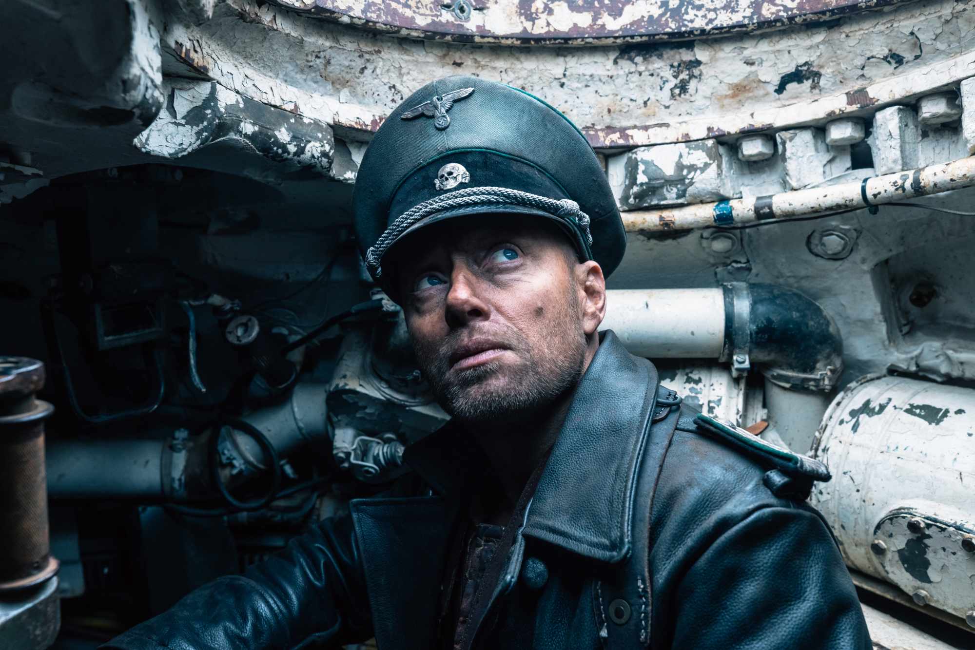 'Sisu' Aksel Hennie as Obersturmführer Bruno Helldorf wearing a Nazi uniform inside of a tank, looking up toward the hole.