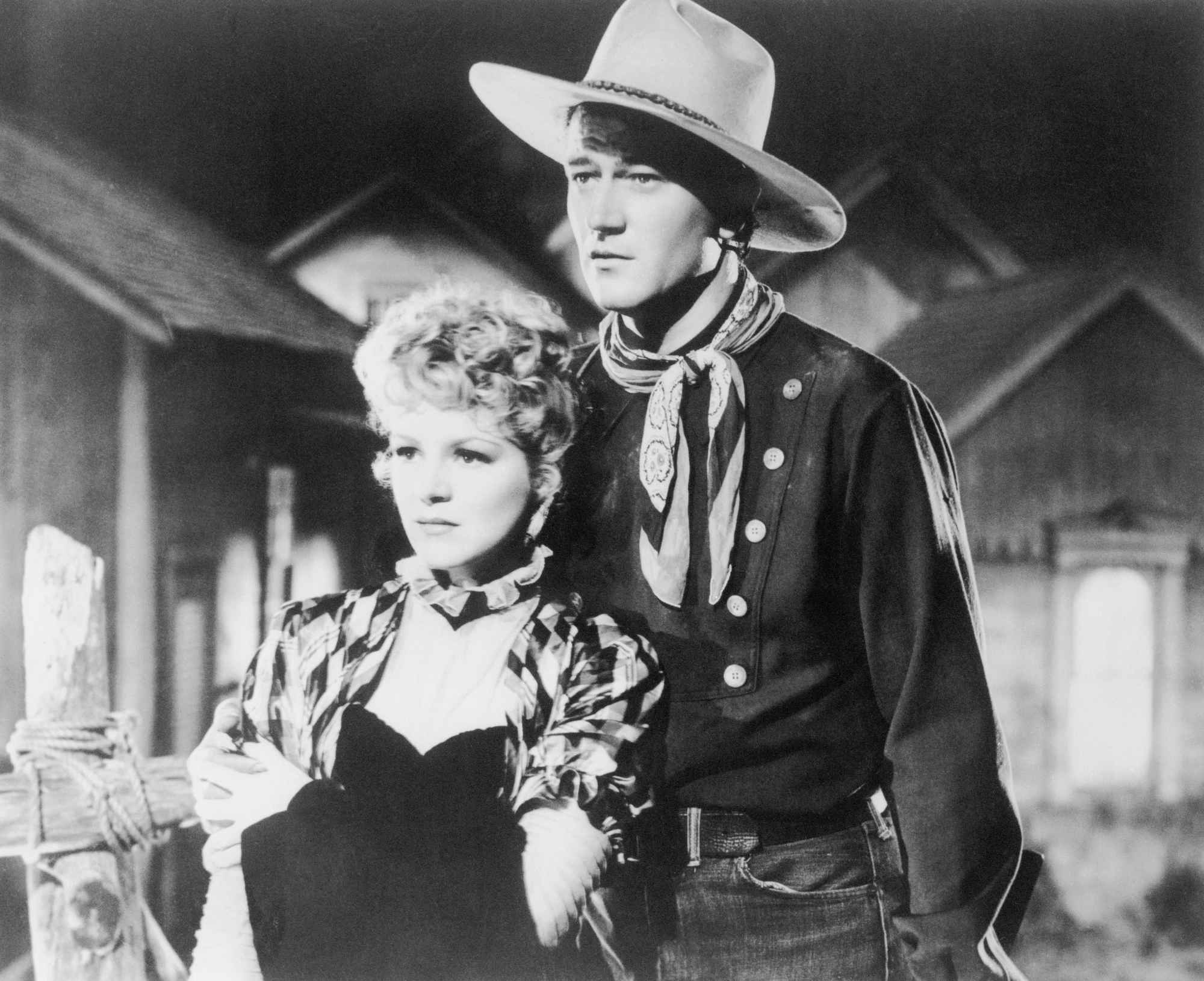 'Stagecoach' Claire Trevor as Dallas and John Wayne as Ringo Kid in black-and-white movies. He has his arm around her, looking concerned.