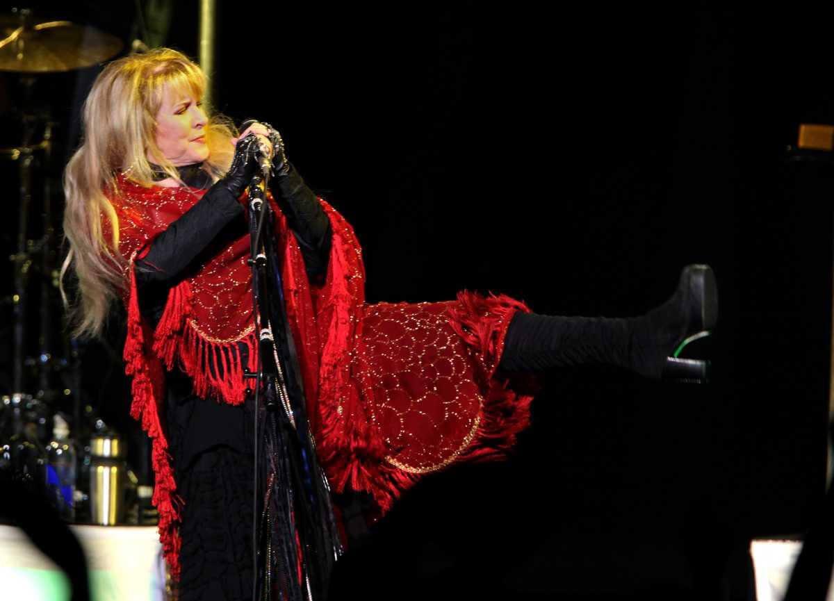 Stevie Nicks wears a red shawl and kicks up her leg.