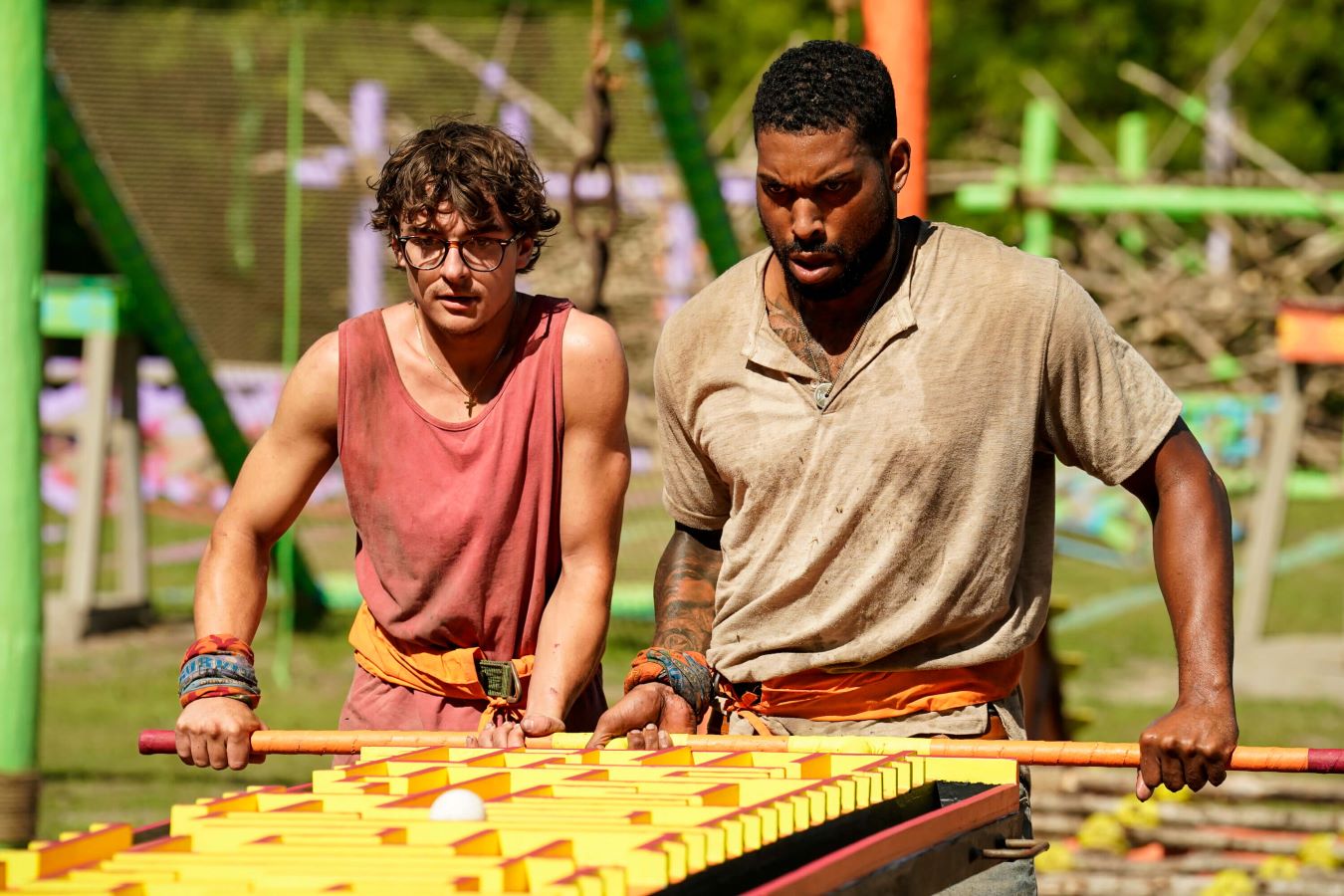 Carson Garrett and Brandon Cottom compete in an Immunity Challenge in 'Survivor 44' on CBS. Carson wears a pink tank top. Brandon wears a light beige long-sleeved shirt.