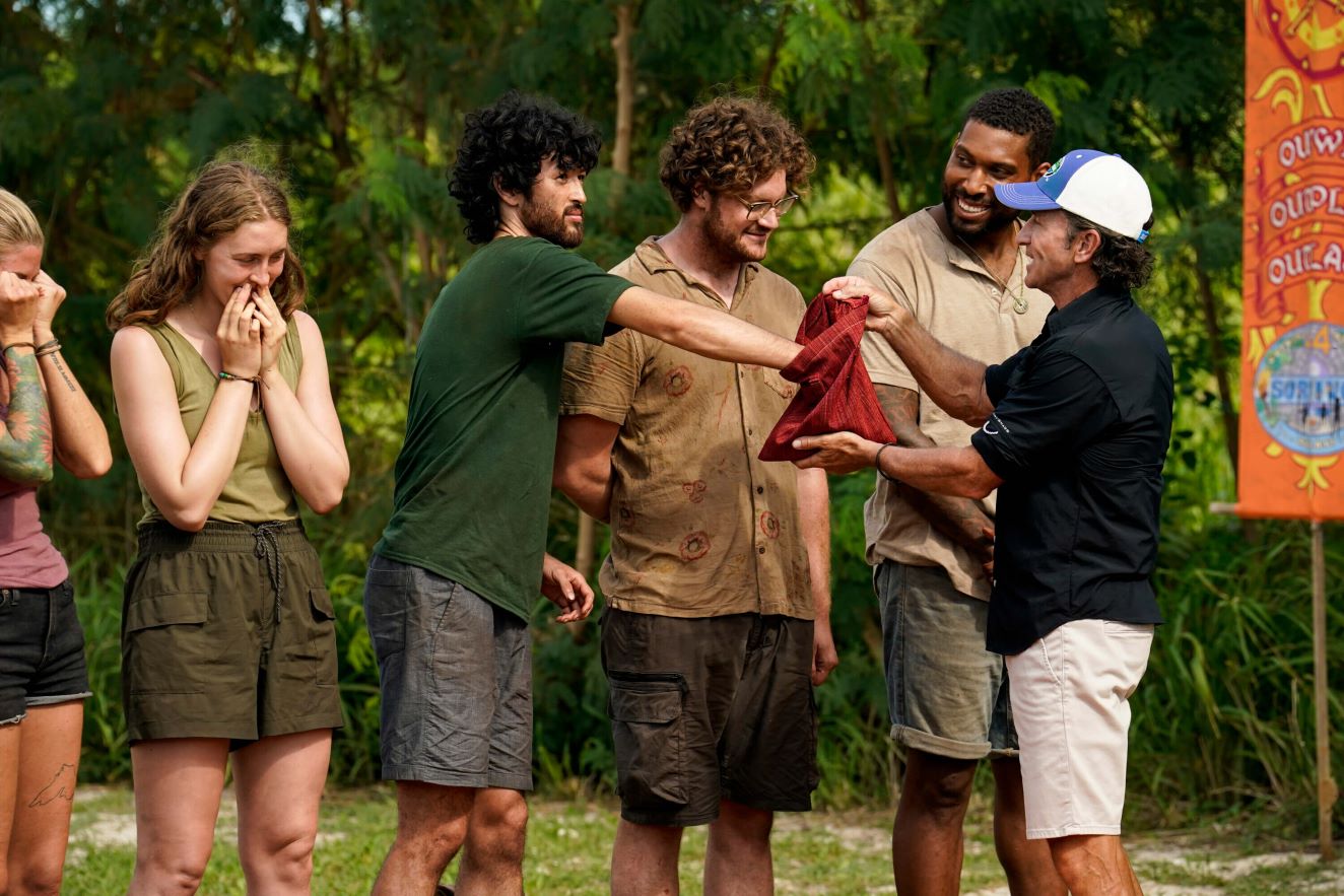 Frannie Marin, Matt Blankinship, Kane Fritzler, Brandon Cottom, and Jeff Probst star in 'Survivor 44' Episode 6, 'Survivor With a Capitol S,' on CBS. In the photo, Probst holds a red bag in front of Matt, and the castaway reaches into it.