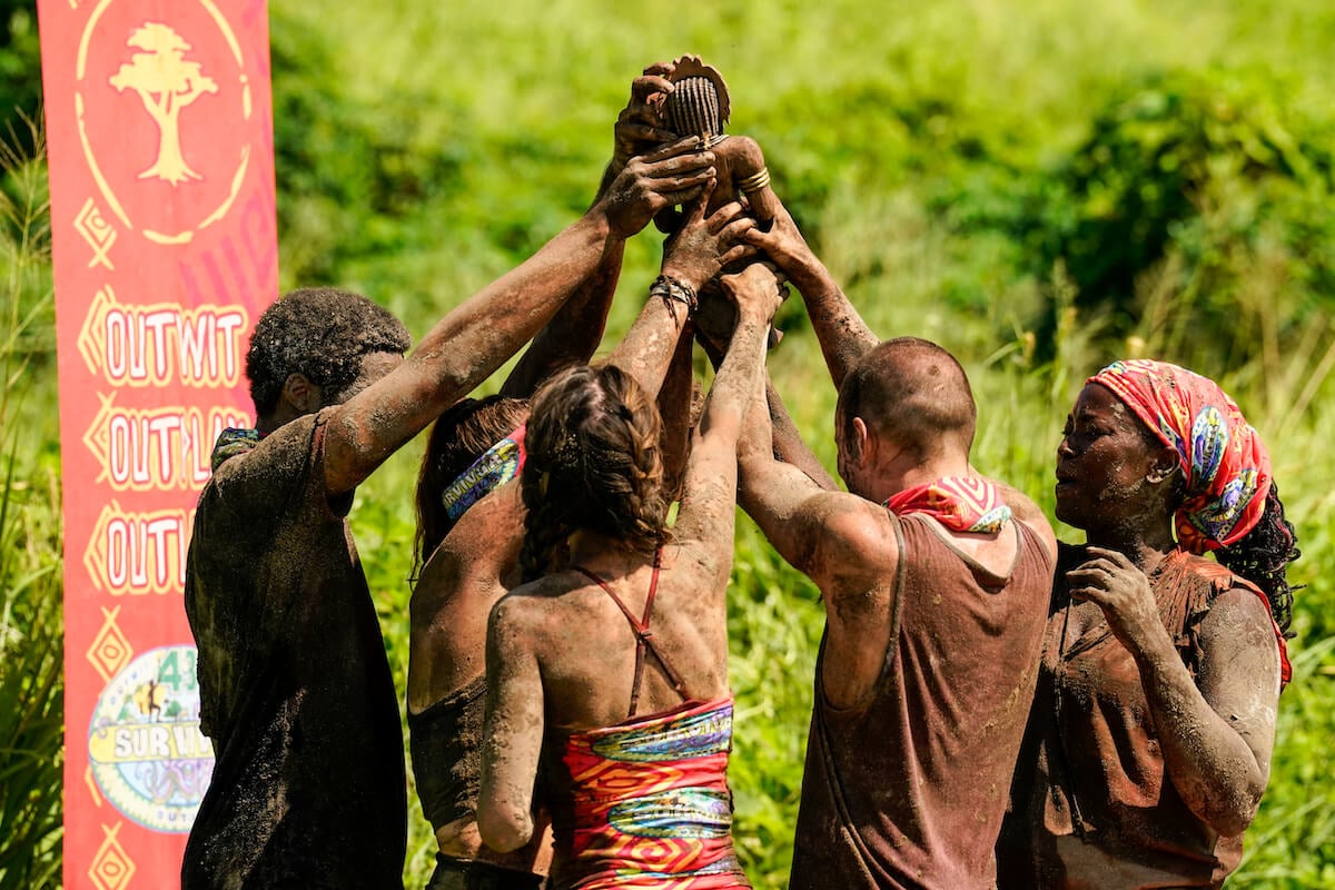 'Survivor' contestants gathering around holding and idol together above them