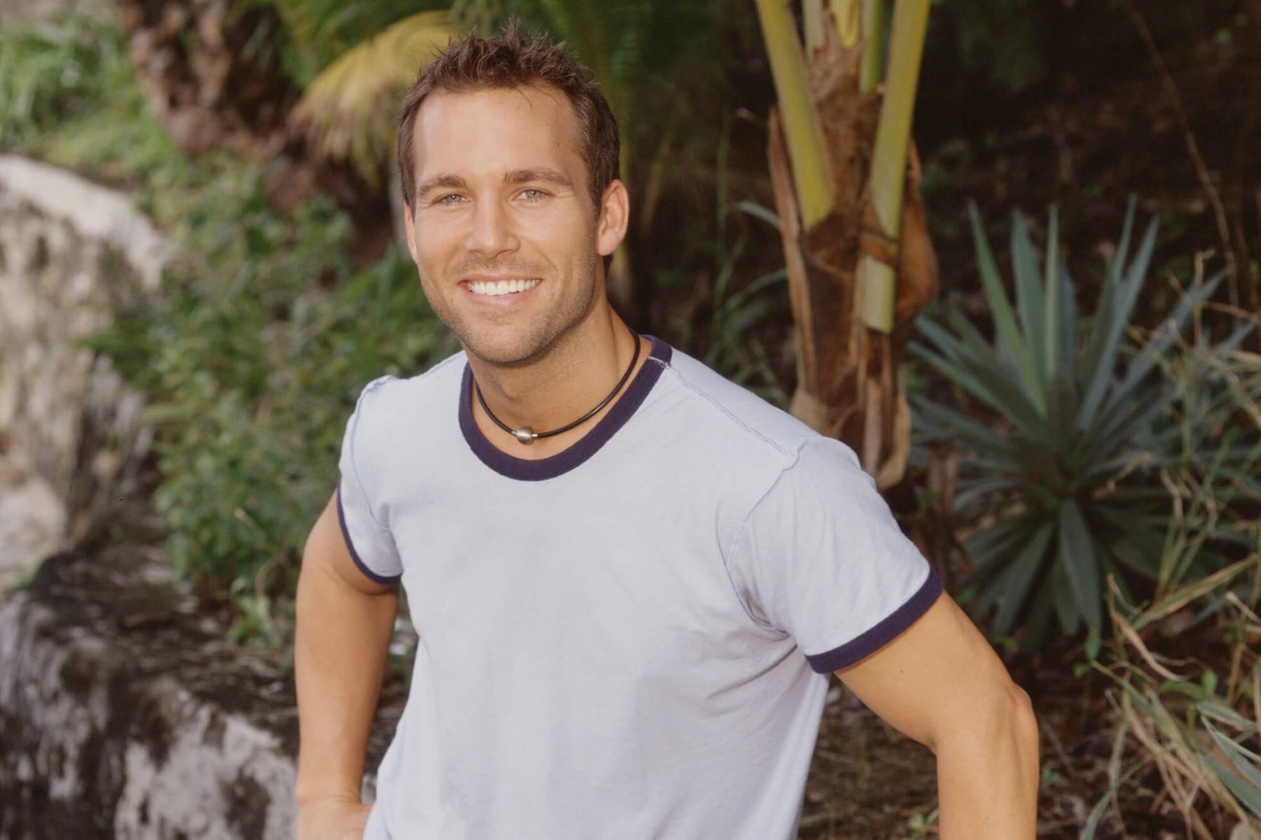 Colby Donaldson, a contestant from 'Survivor' on CBS, wears a light gray t-shirt and leans against a rock wall.