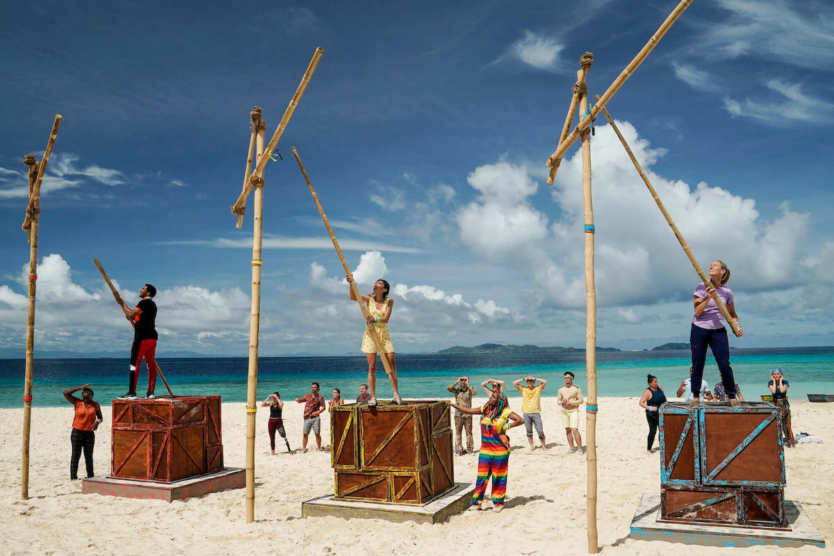 'Survivor' challenge on a beach featuring wooden blocks and bamboo poles