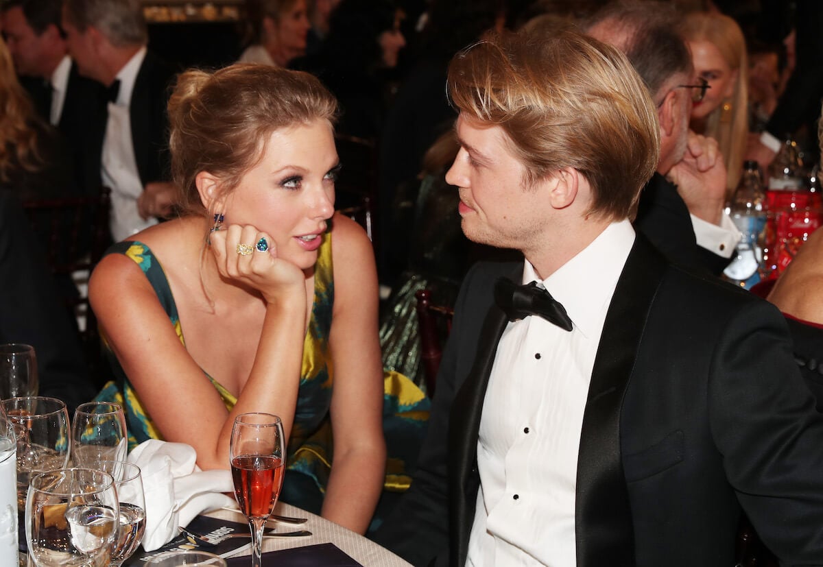 Taylor Swift and Joe Alwyn sitting next to each other and looking at each other