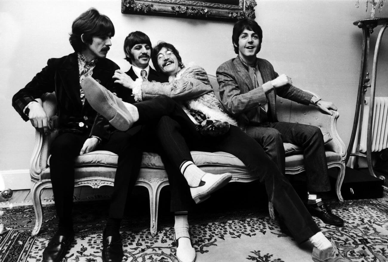 A black and white picture of George Harrison, Ringo Starr, John Lennon, and Paul McCartney sitting on a couch together.