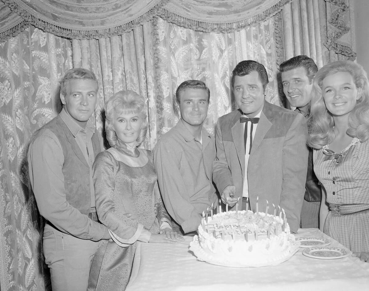 Cast members of 'The Big Valley' standing behind a table with a cake on it