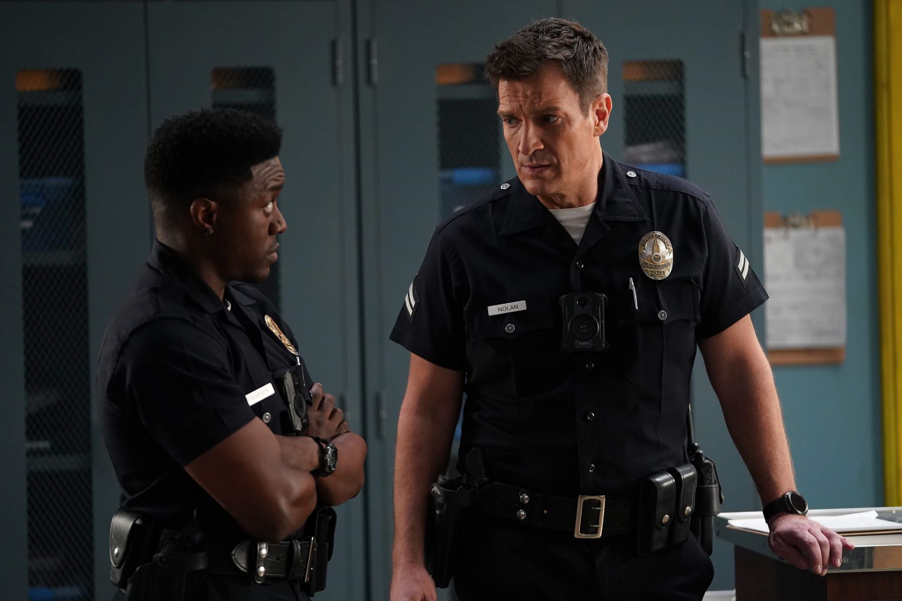 Tru Valentino as Aaron Thorsen and Nathan Fillion as John Nolan, who will both appear in the season 5 finale of 'The Rookie,' share a scene in episode 13, 'Daddy Cop.' They both wear their dark blue cop uniforms.