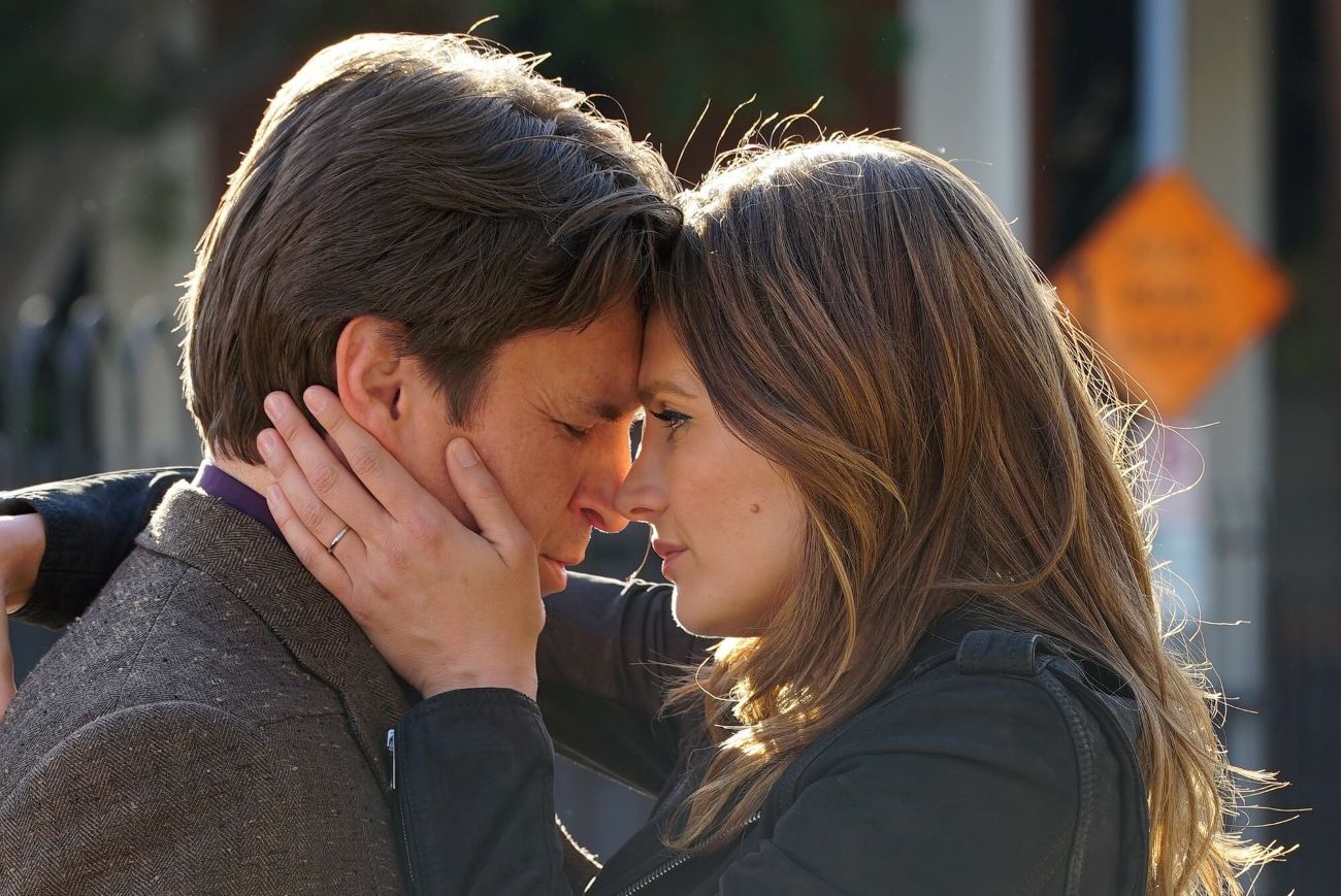 Nathan Fillion, who currently stars in the ABC show 'The Rookie,' shares a scene with Stana Katic in 'Castle.' Their characters, Castle and Beckett, embrace in the photo. Castle wears a gray tweed coat. And Beckett wears a black jacket.