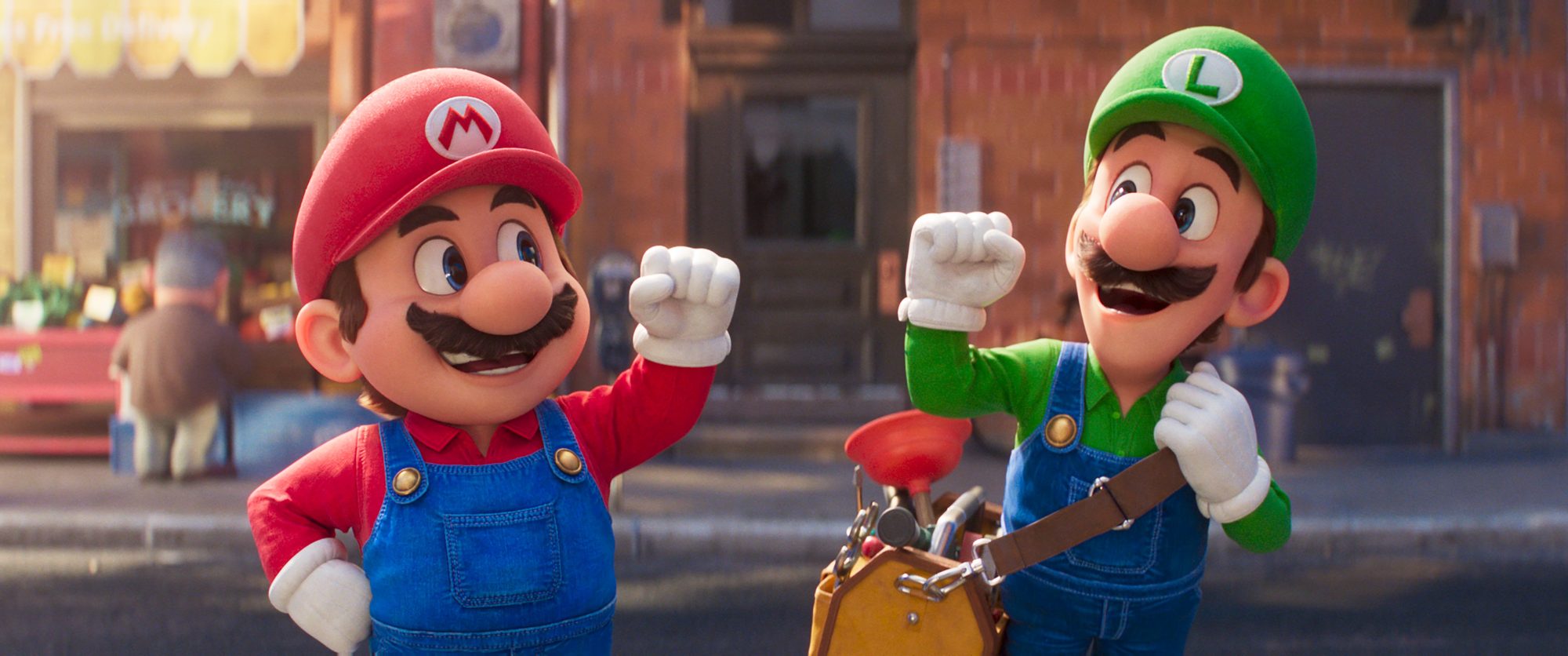 'The Super Mario Bros. Movie' Mario (voiced by Chris Pratt) and Luigi (voiced by Charlie Day) holding up their fists into the air in front of a brick building. Luigi has a bag of plumbing tools.