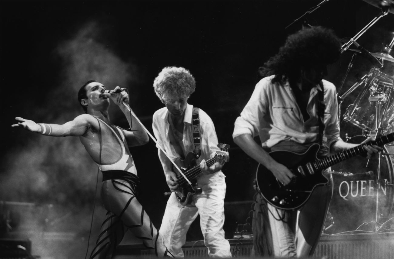 A black and white picture of Freddie Mercury, John Deacon, and Brian May of Queen performing in concert.