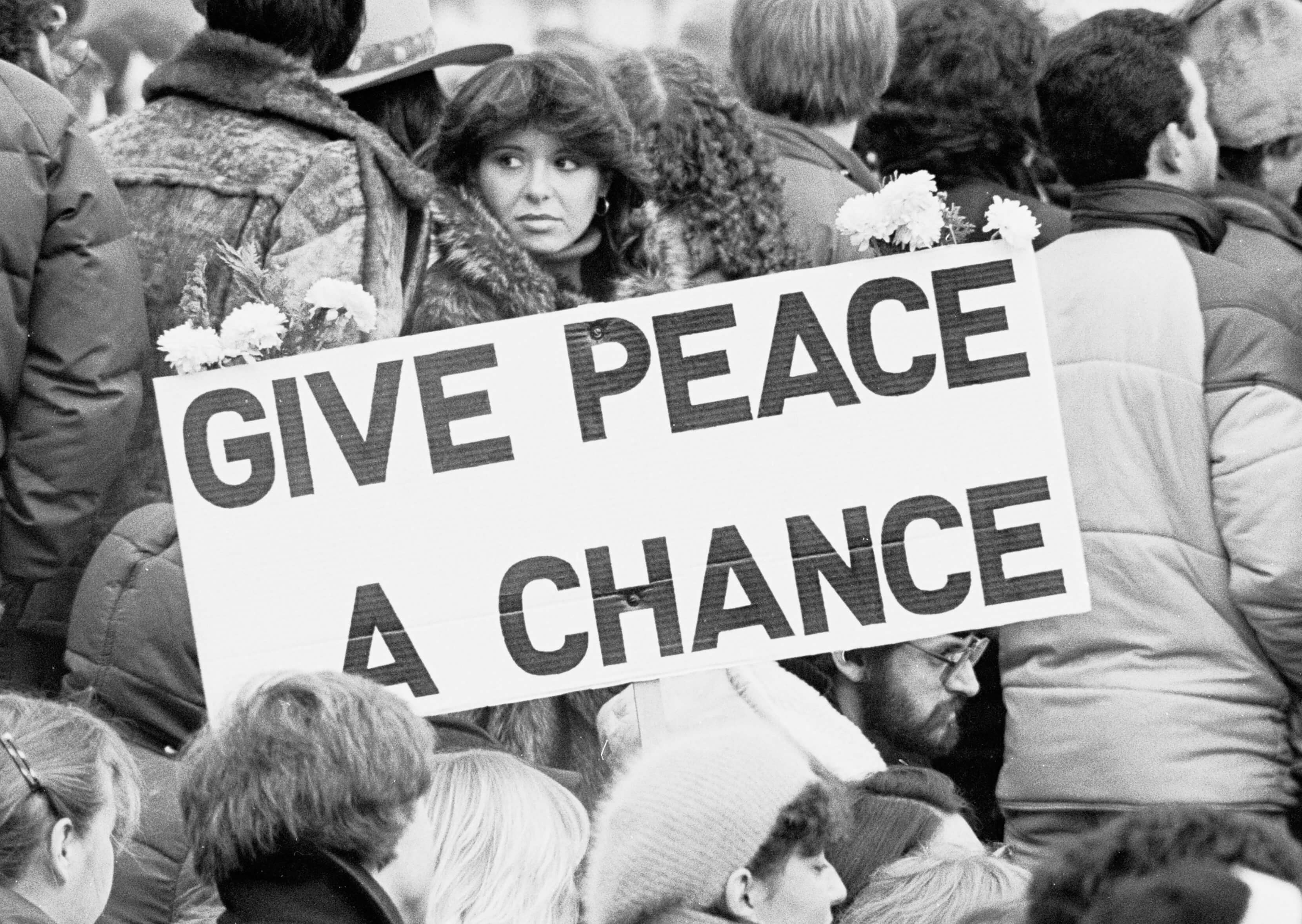 A black-and-white photo of a sign referencing John Lennon's "Give Peace a Chance"