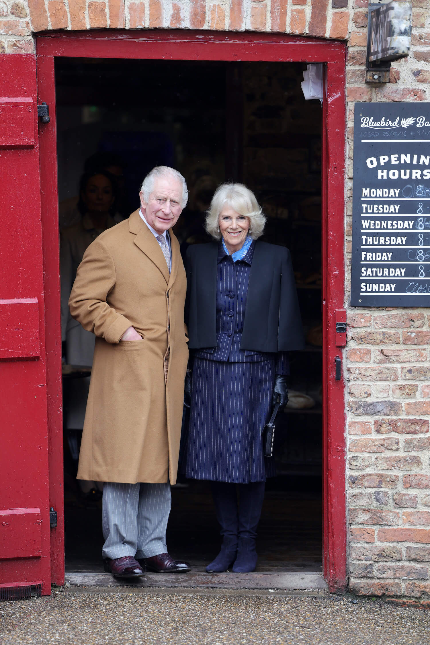 Full length shot of King Charles and Queen Camilla posing in a doorway wearing coats