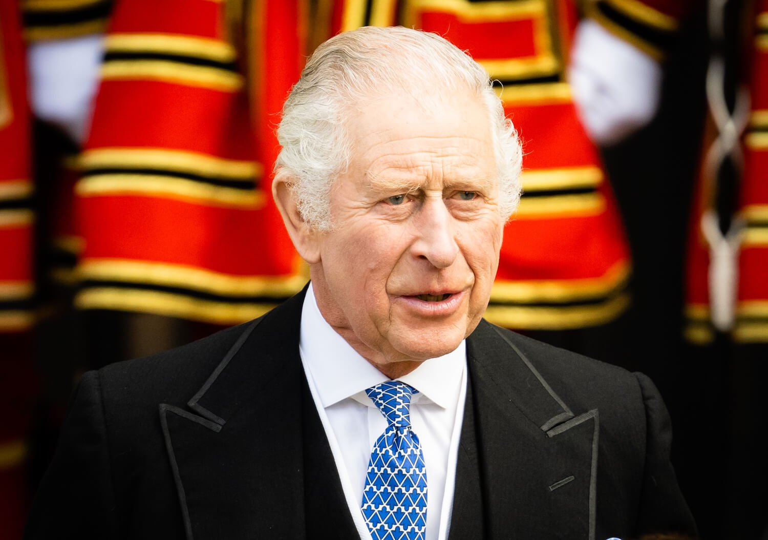 King Charles wears a dark suit and tie while looking off