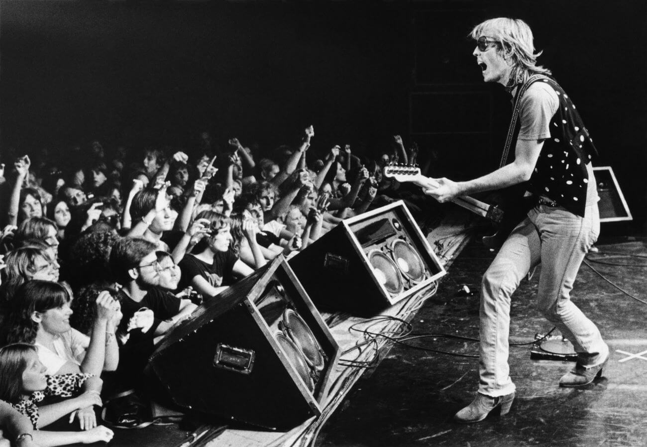 A black and white picture of Tom Petty playing guitar in front of an audience.