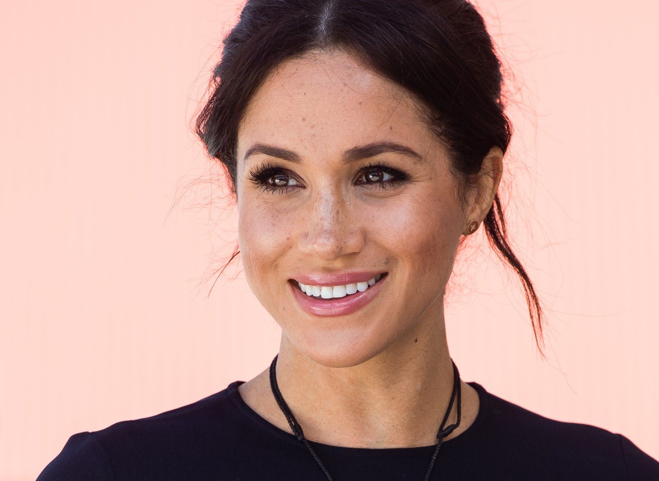 Meghan Markle smiles while wearing a black dress.