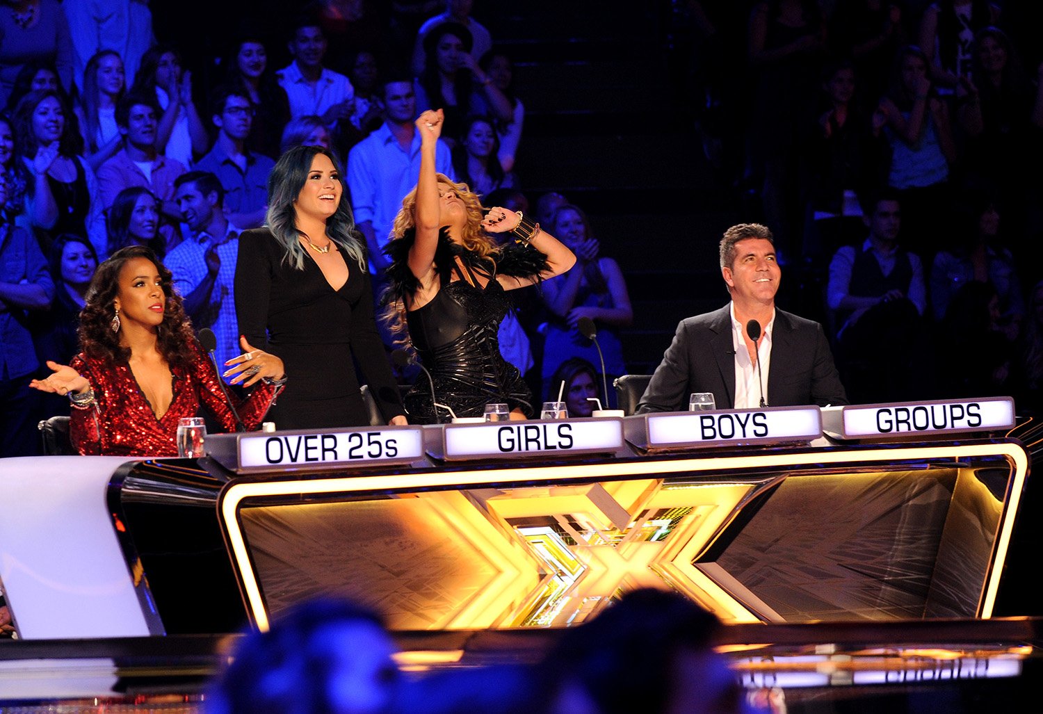 X Factor USA: Kelly Rowland, Demi Lovato, Paulina Rubio and Simon Cowell smiling and cheering at the judges' table.