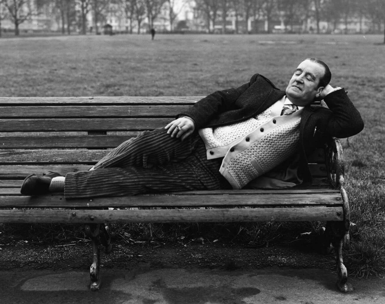 A black and white picture of Alfred Lennon laying on a bench.
