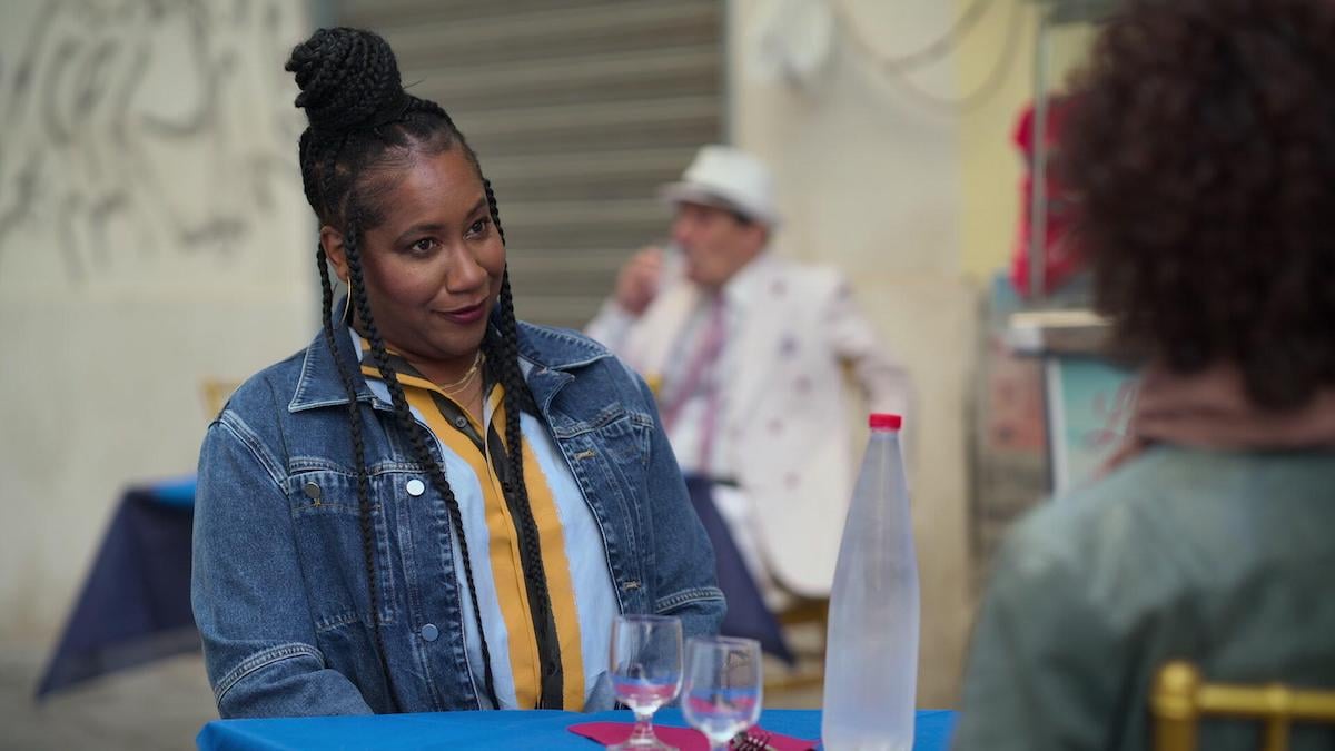 Chef Alisa Reynolds wearing a denim jacket and sitting at a table in 'Searching for Soul Food'