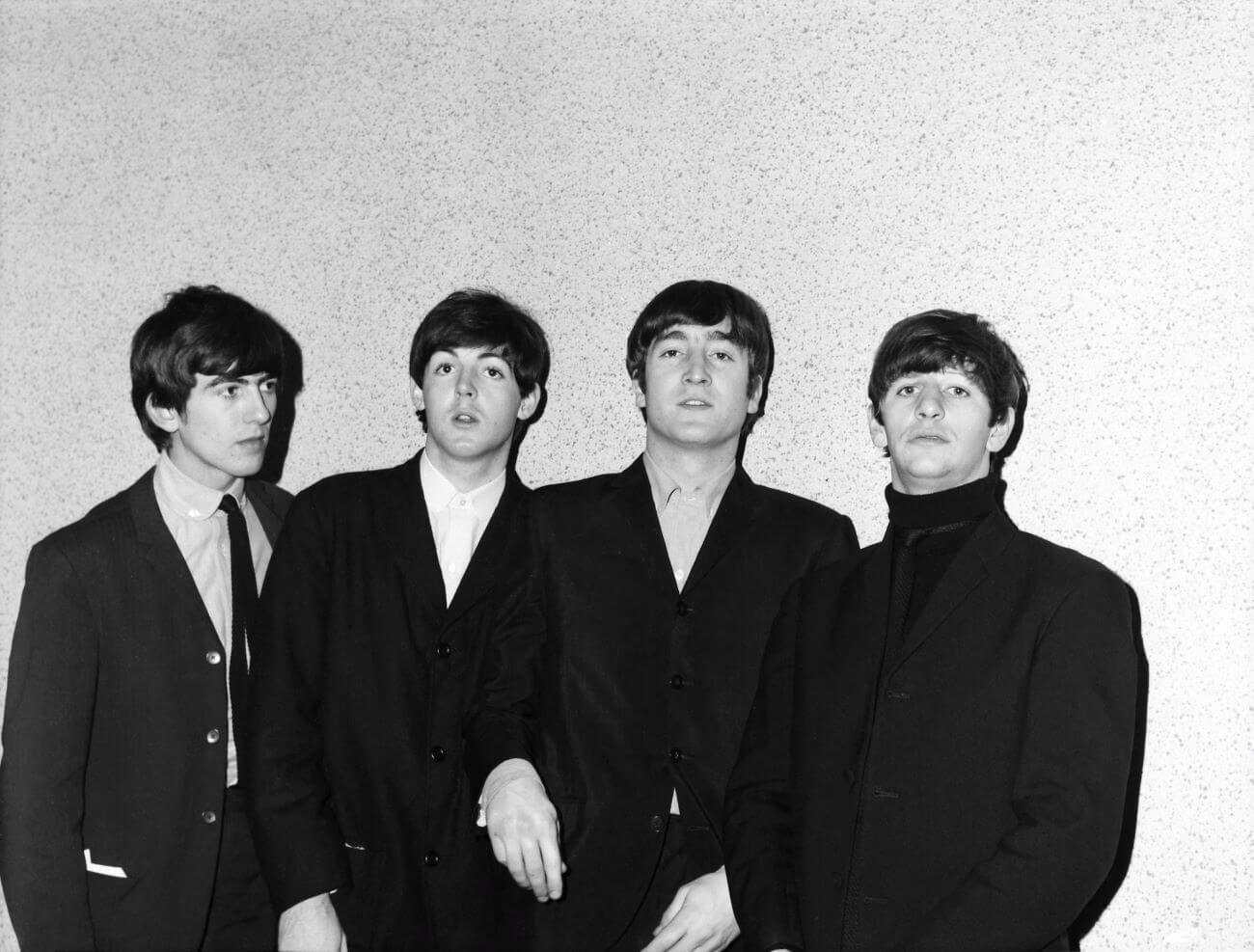 A black and white picture of George Harrison, Paul McCartney, John Lennon, and Ringo Starr of The Beatles wearing black and posing against a white wall.