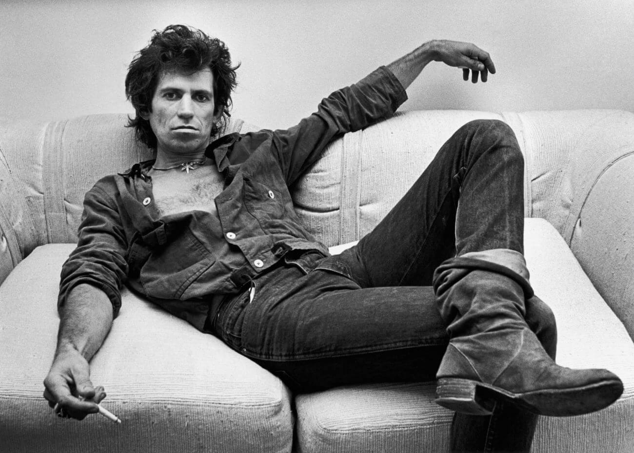A back and white picture of Keith Richards sprawled on a couch with a cigarette in his hand.