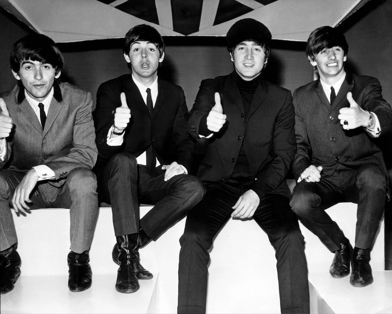 Beatles members (from left) George Harrison, Paul McCartney, John Lennon, and Ringo Starr wearing suits and giving thumbs up signs.