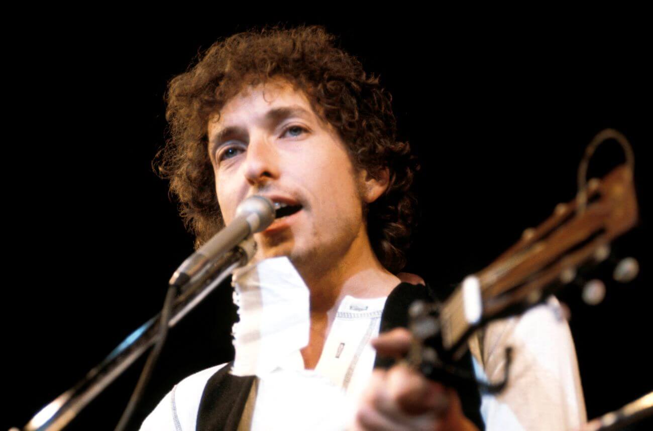 Bob Dylan plays guitar and sings into a microphone.