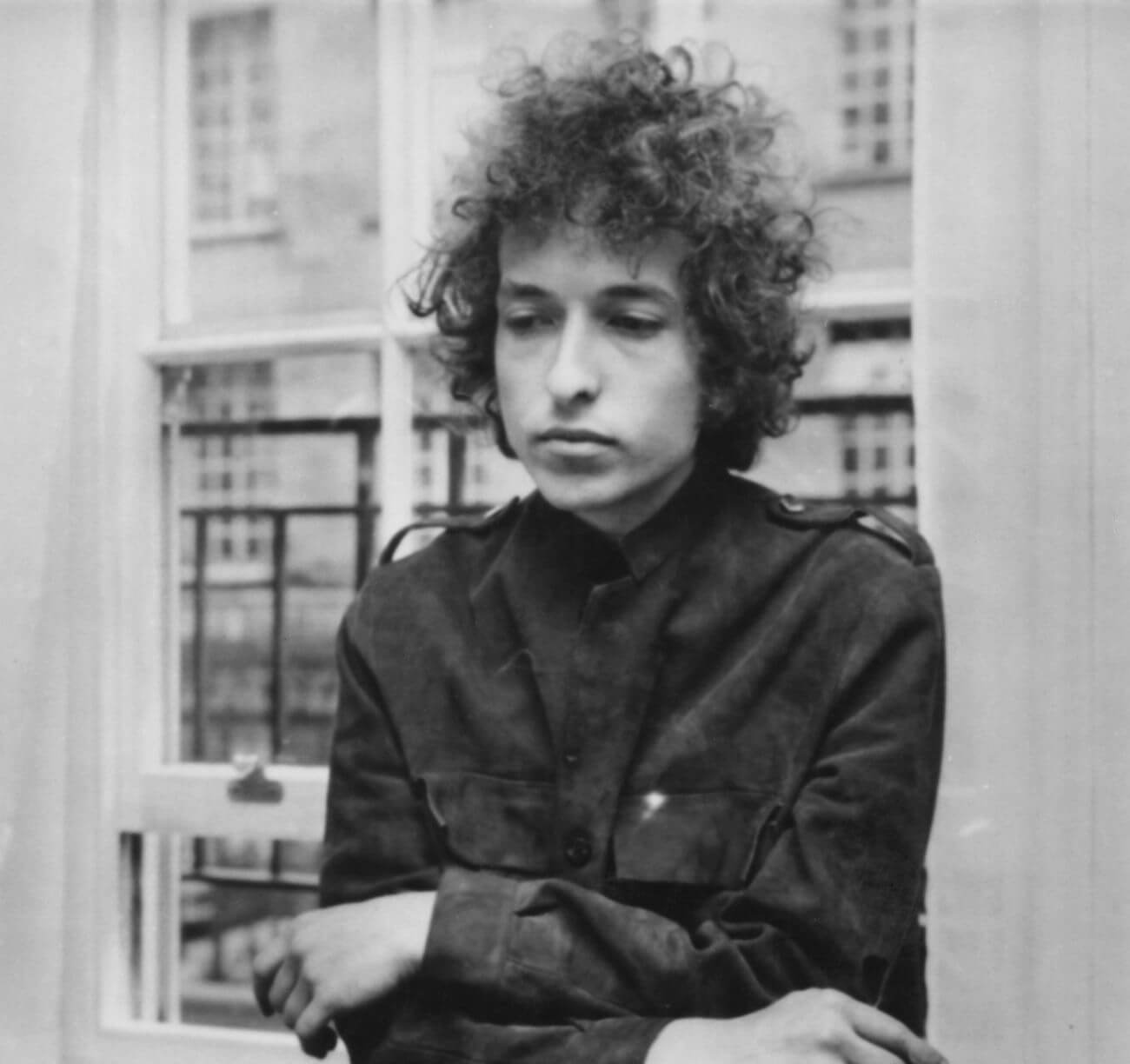 A black and white picture of Bob Dylan leaning against a window.